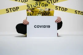 Police STOP tape infront of a human being holding up a sign saying COVID19