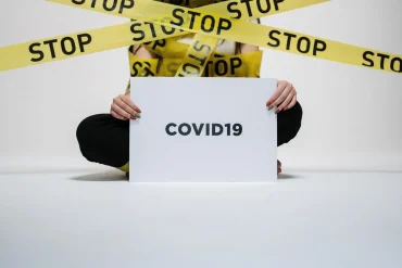Police STOP tape infront of a human being holding up a sign saying COVID19
