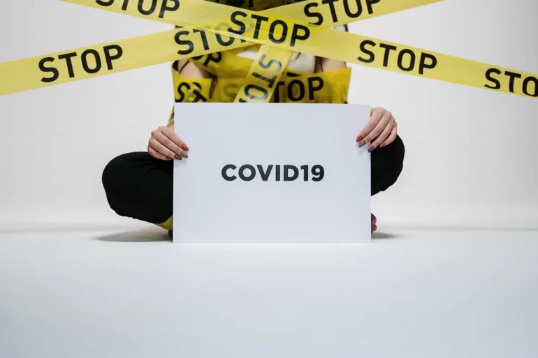 Police STOP tape infront of a human being holding up a sign saying COVID19