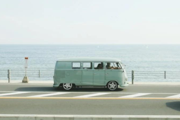 Pastels image of a volkswagen camper parked up on a road next to the water.
